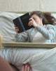 A young woman reading in the bottom of a bunk bed. Another person opens a storage drawer on the side and then the bottom of a bunk bed. Another tucks in the sheets of a bed.